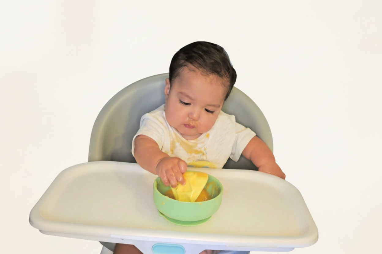 Baby in a high chair with a bowl and spoon on a white background